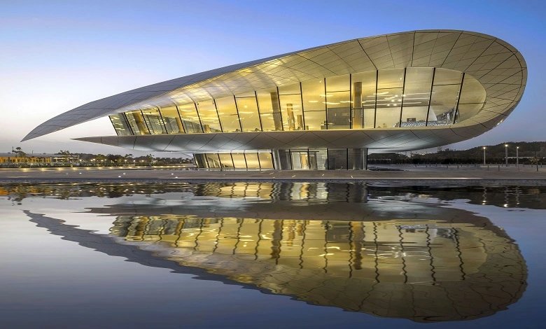 Modern elliptical glass building with warm lighting reflected in water at twilight—Dubai's Etihad Museum.