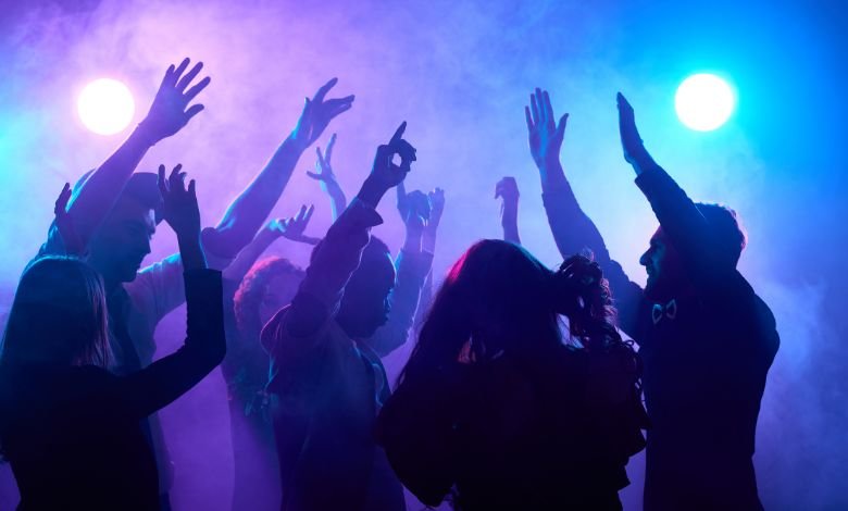 Group of people dancing at a nightclub with colorful lights and smoke in the background