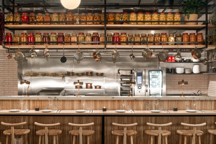 Interior of Amber Restaurant featuring a counter with wooden stools, shelves with jars of preserved foods, and a professional kitchen setup in the background.