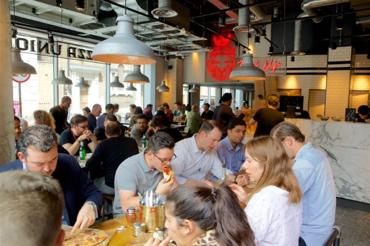Interior of a bustling Pizza Union restaurant with customers enjoying their meals at communal tables.