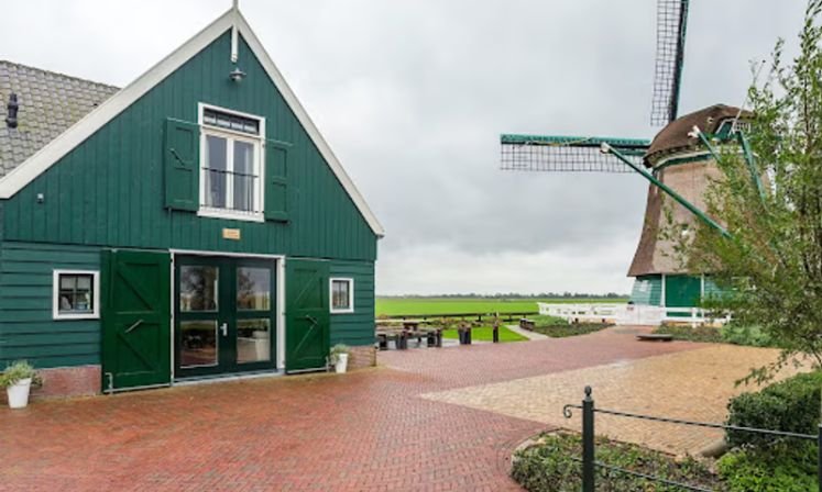 A green house with a windmill in the background, featuring Middenbeemster Serviced Apartments for group accommodation.