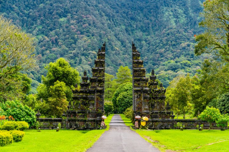 Traditional Balinese gate with people carrying offerings at a temple, Indonesia