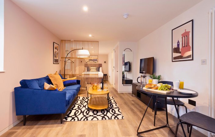 Modern serviced apartment with blue sofa and breakfast table.