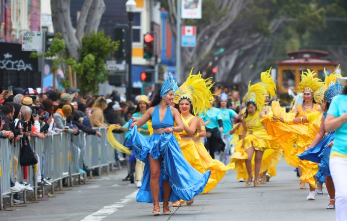 Notting Hill Carnival street parade with dancers in colorful blue and yellow costumes.