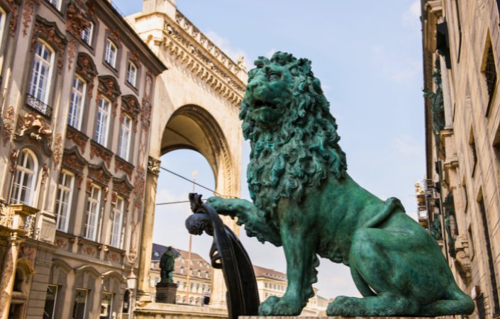 Close-up of a bronze lion statue in Munich’s Old Town, highlighting intricate architectural details in the background.