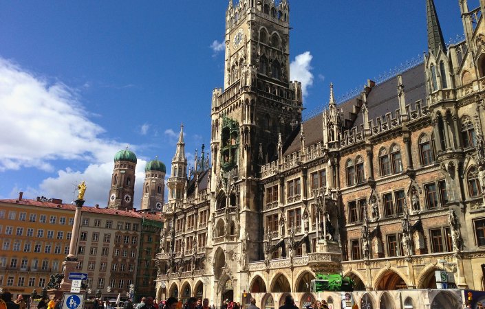 Daytime view of Munich city center with Frauenkirche cathedral and Marienplatz, highlighting red rooftops and blue skies.