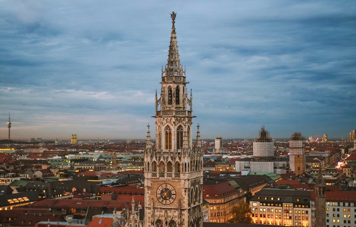Evening cityscape of Munich with the spire of the New Town Hall tower under a moody sky.  Image 6: Daytime view of Munich city center with Frauenkirche cathedral and Marienplatz, highlighting red rooftops and blue skies.  Image 7: Modern serviced apartment interior in Munich featuring an open-plan kitchen, dining table, and cozy living space.  If you want them shorter or more descriptive, just let me know! 