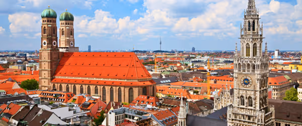 Daytime view of Munich city center with Frauenkirche cathedral and Marienplatz, highlighting red rooftops and blue skies.