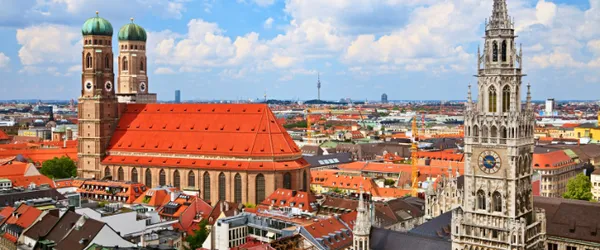 Daytime view of Munich city center with Frauenkirche cathedral and Marienplatz, highlighting red rooftops and blue skies.