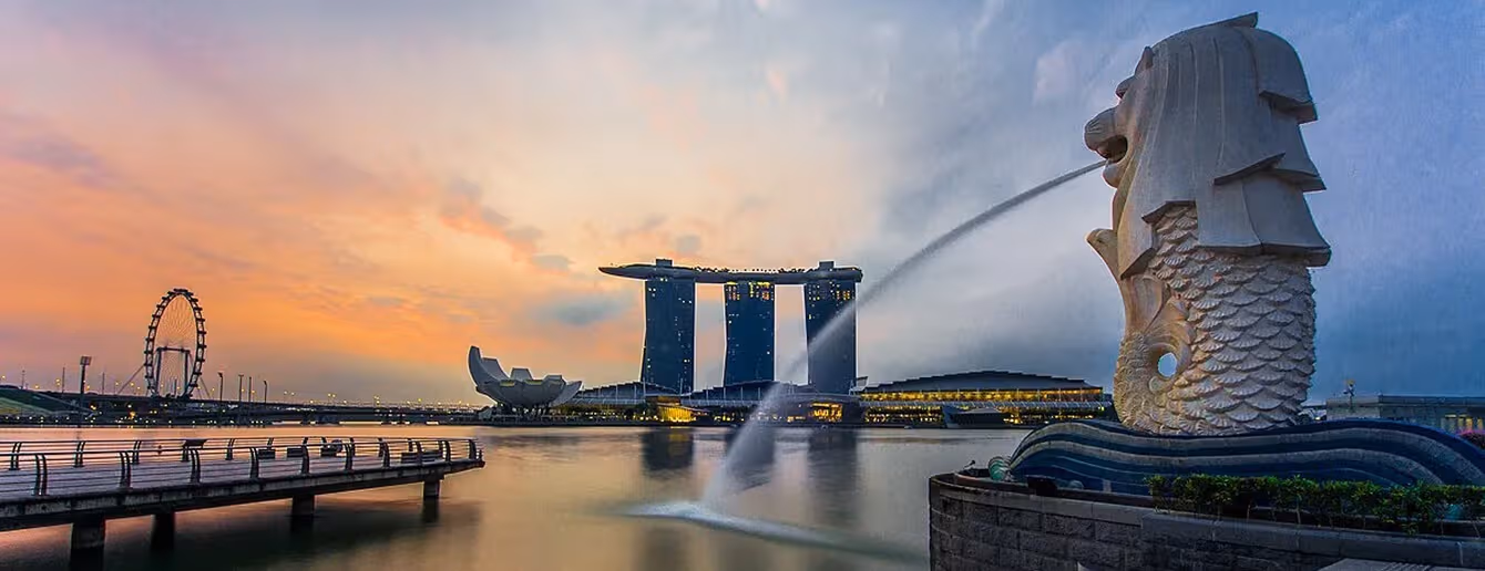 Singapore skyline view with Merlion statue, Marina Bay Sands, waterfront, and nearby holiday apartments at sunset.